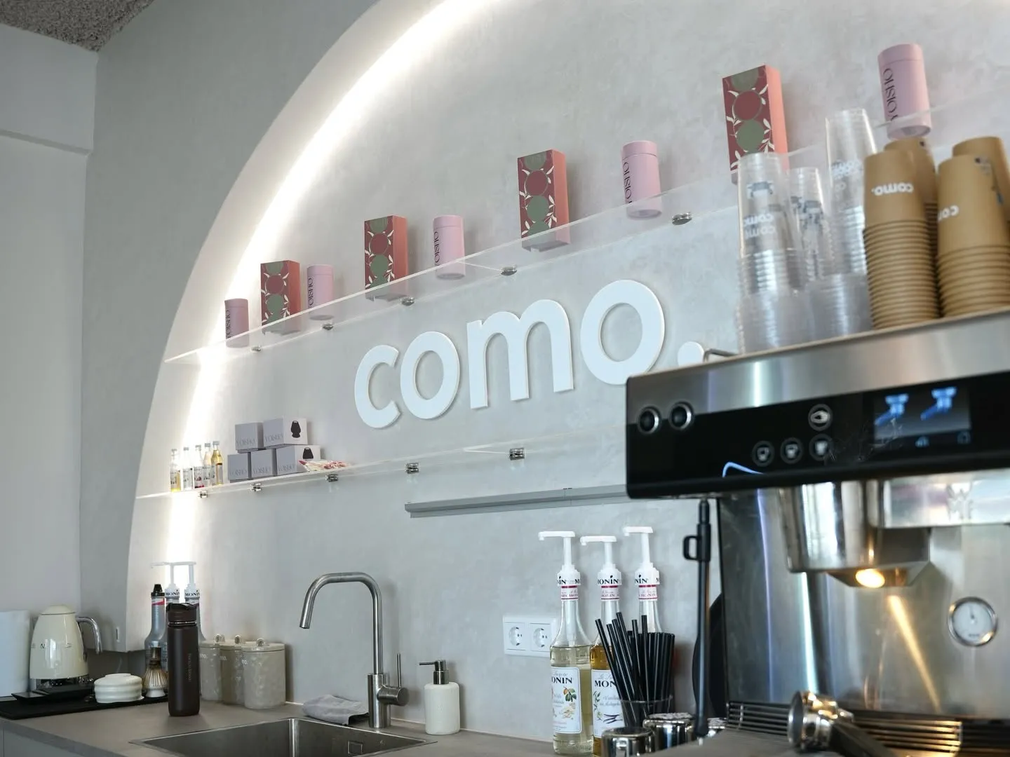 De bar van COMO met de verlichte boog in de wand, het logo en de matchablikken op de planken