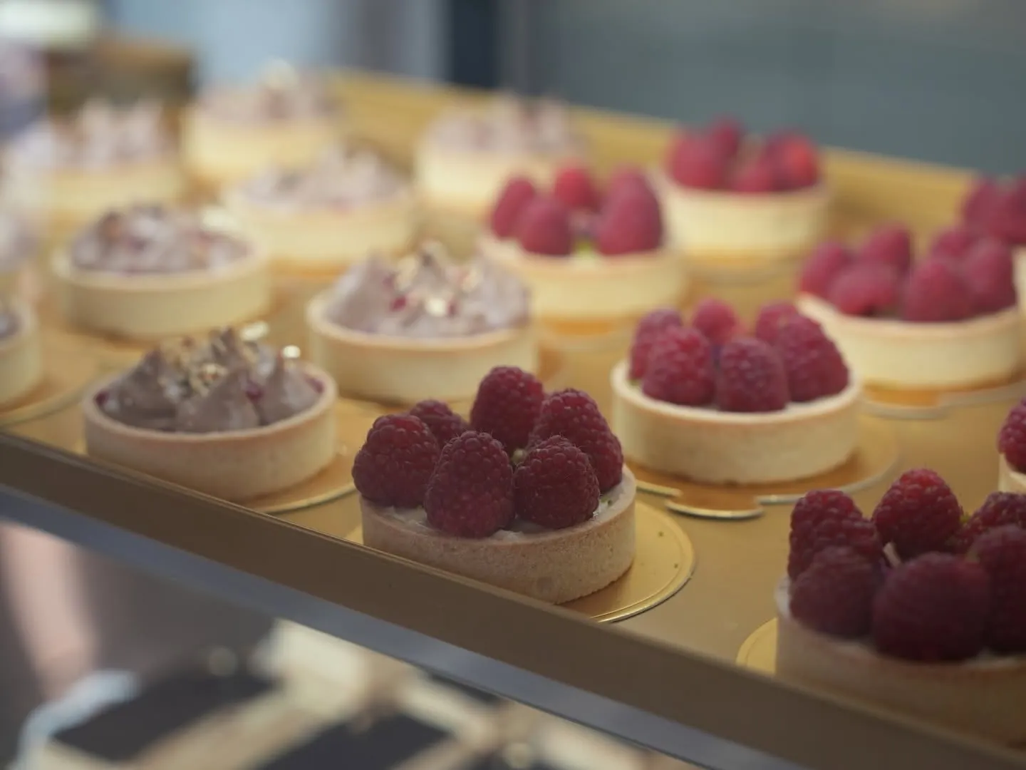 Frambozentaartjes op gouden schaaltjes in de verlichte vitrine van COMO